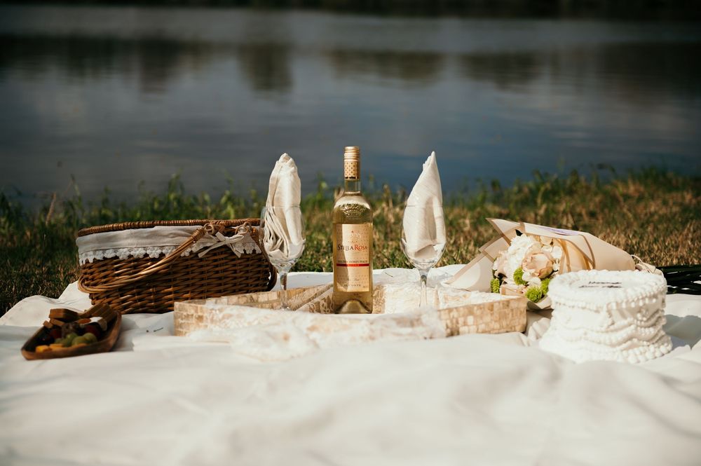 Panoramic view of wine bottles and glassware arranged on white linen against a lakeside background.