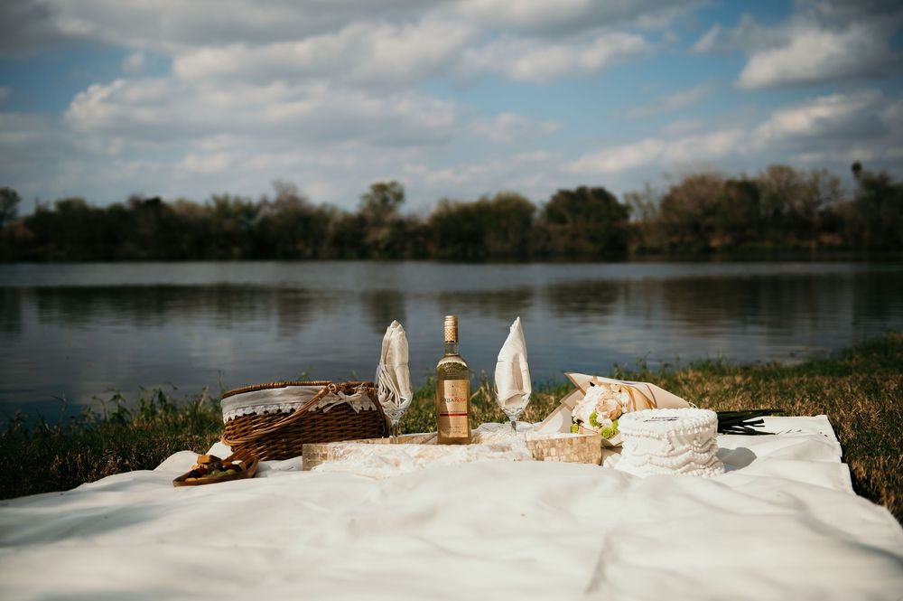 A romantic picnic setup with champagne glasses and snacks on a white blanket beside a serene lake.