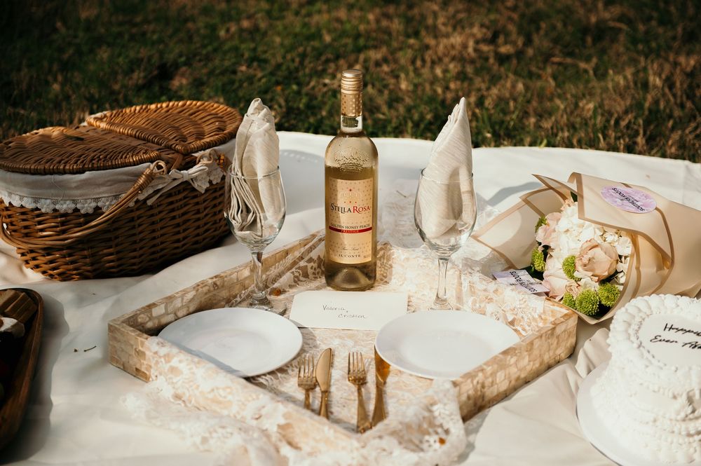 An elegant outdoor picnic setup with white linens, wicker baskets, and wine glasses.