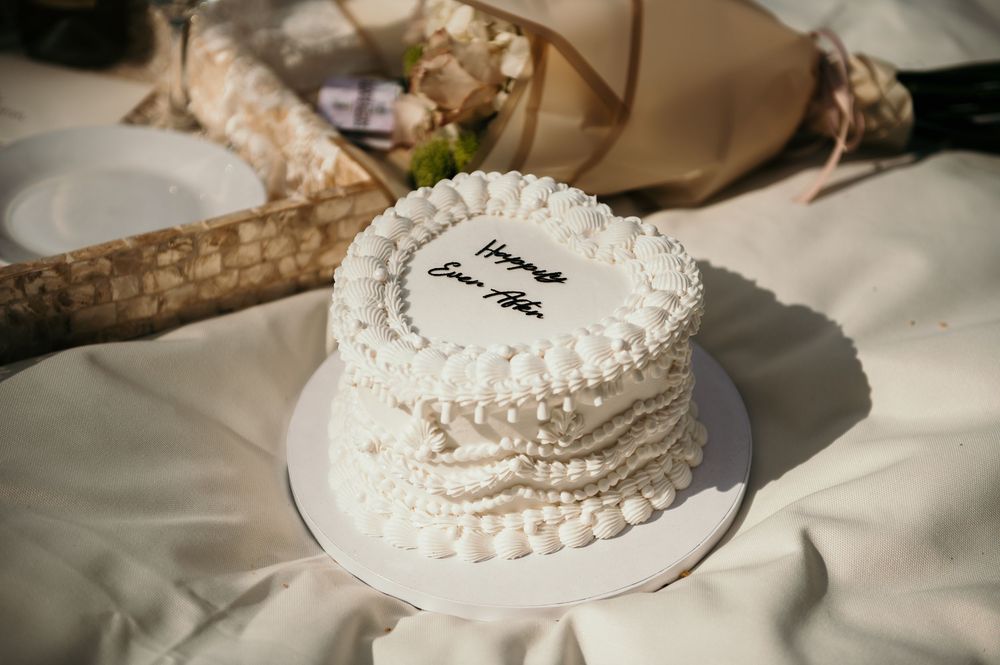 White wedding cake with delicate pearl decorations displayed on a lace-covered table.