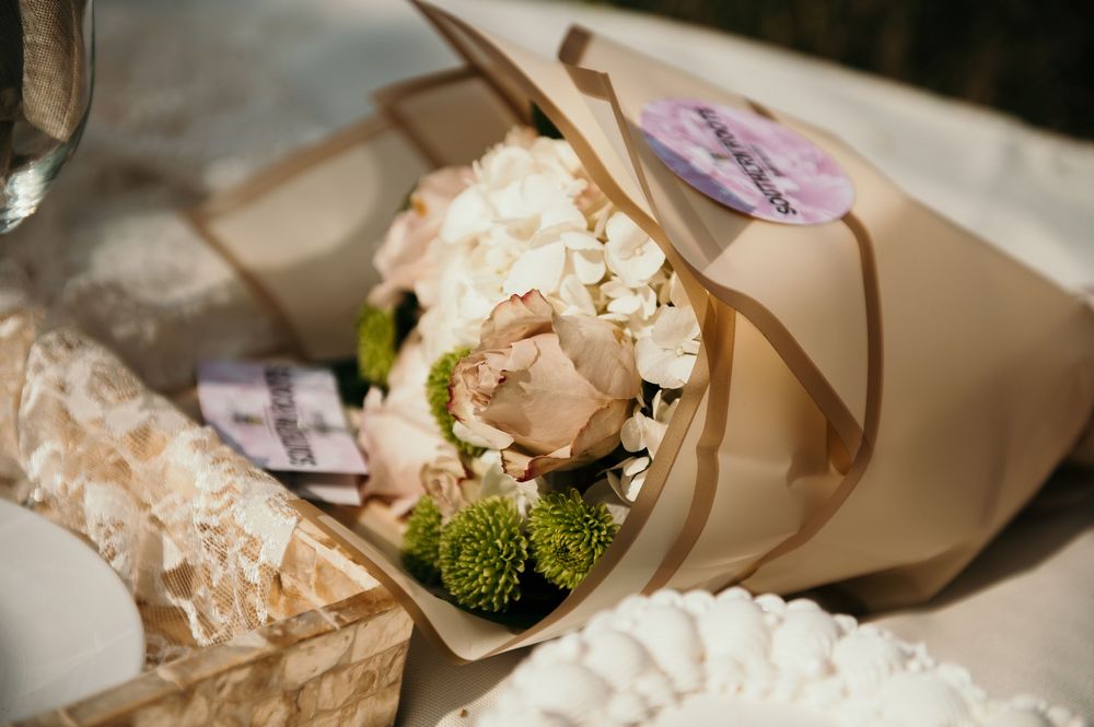A delicate floral bouquet with white roses and greenery wrapped in kraft paper.