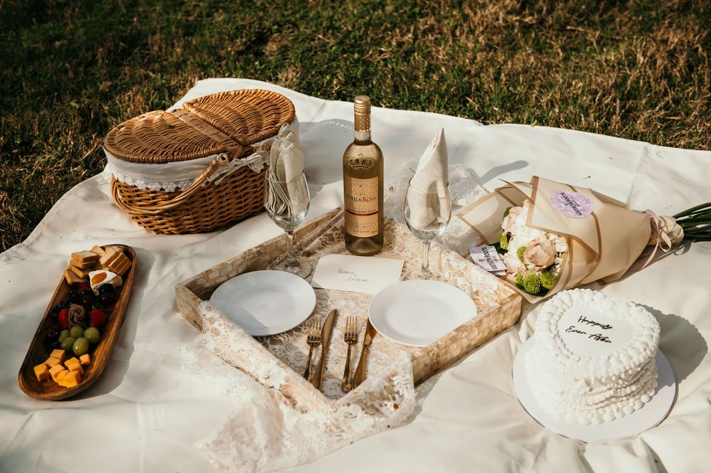 Rustic outdoor picnic spread with wine, bread, and table settings laid out on a white blanket.