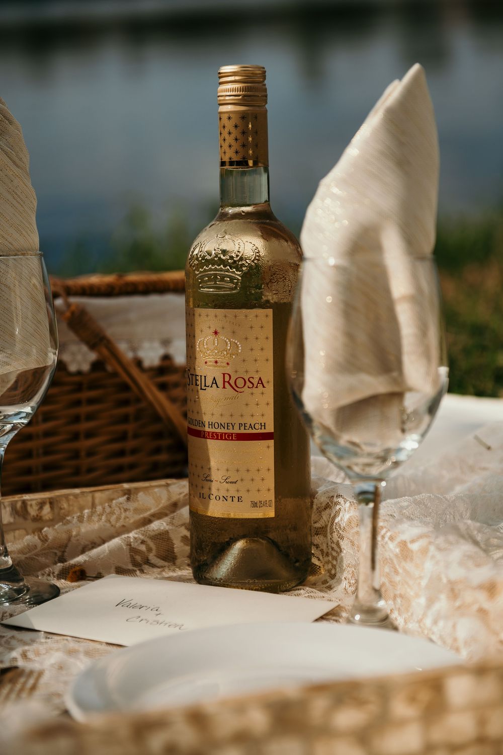 A bottle of Alba Rosa wine sits on a picnic setup with wine glasses and basket.