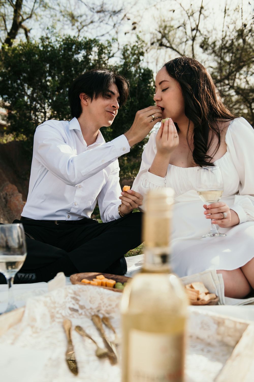Sequence of intimate picnic moments showing couple in white clothing feeding each other against natural backdrop.