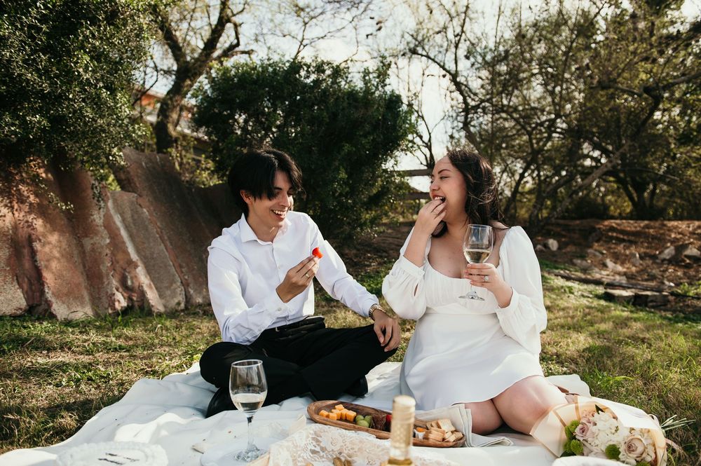 Couple enjoys romantic outdoor picnic with wine and snacks on white blanket during golden hour.