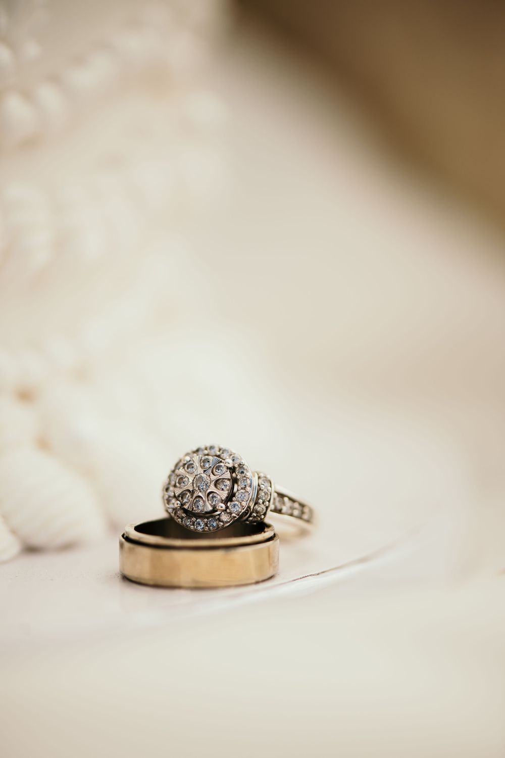 Wedding rings on white fabric featuring an ornate diamond halo engagement ring and plain gold wedding band.