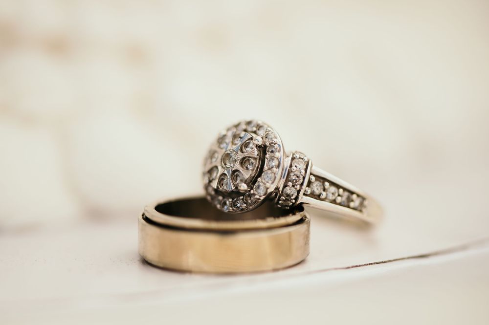 A sparkling diamond engagement ring and gold wedding band rest together on a cream colored surface.
