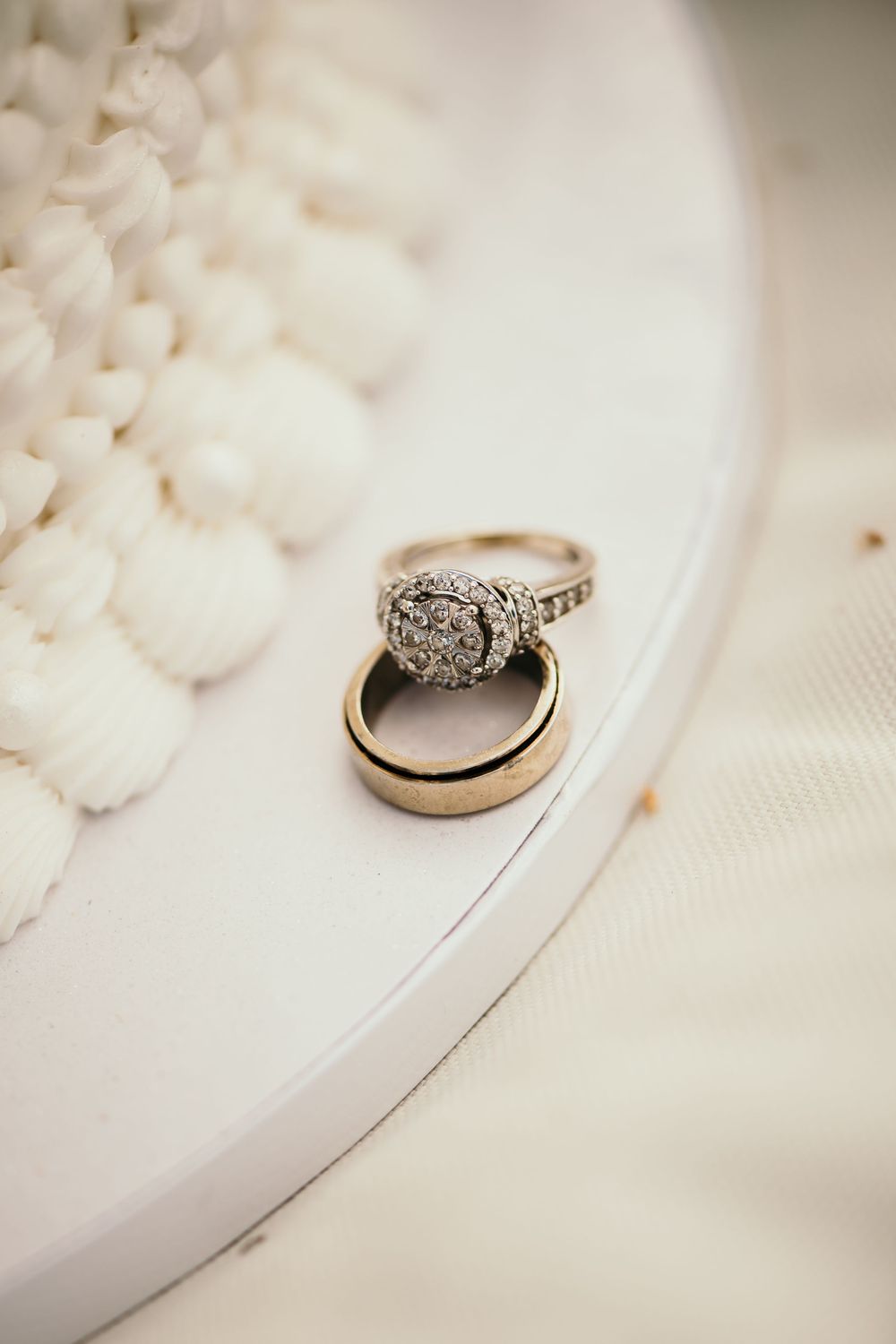 Wedding rings with a diamond engagement ring resting on a white textured surface in soft lighting.