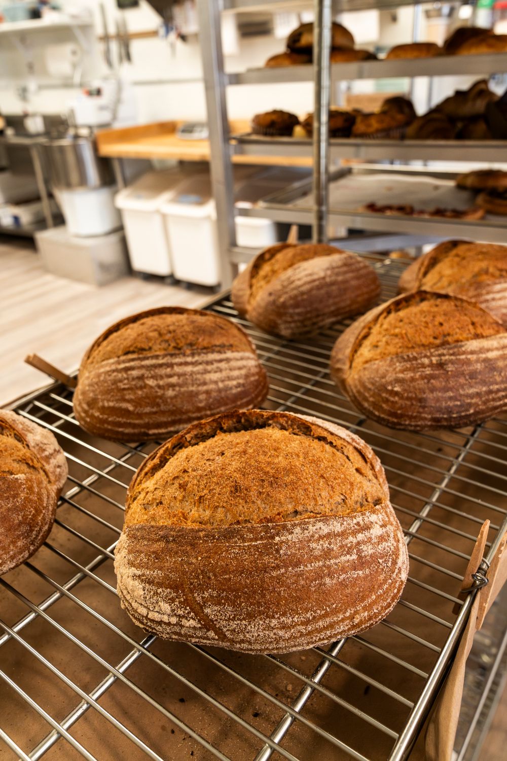 Rustic sourdough bread loaves cooling on wire racks in a commercial kitchen.