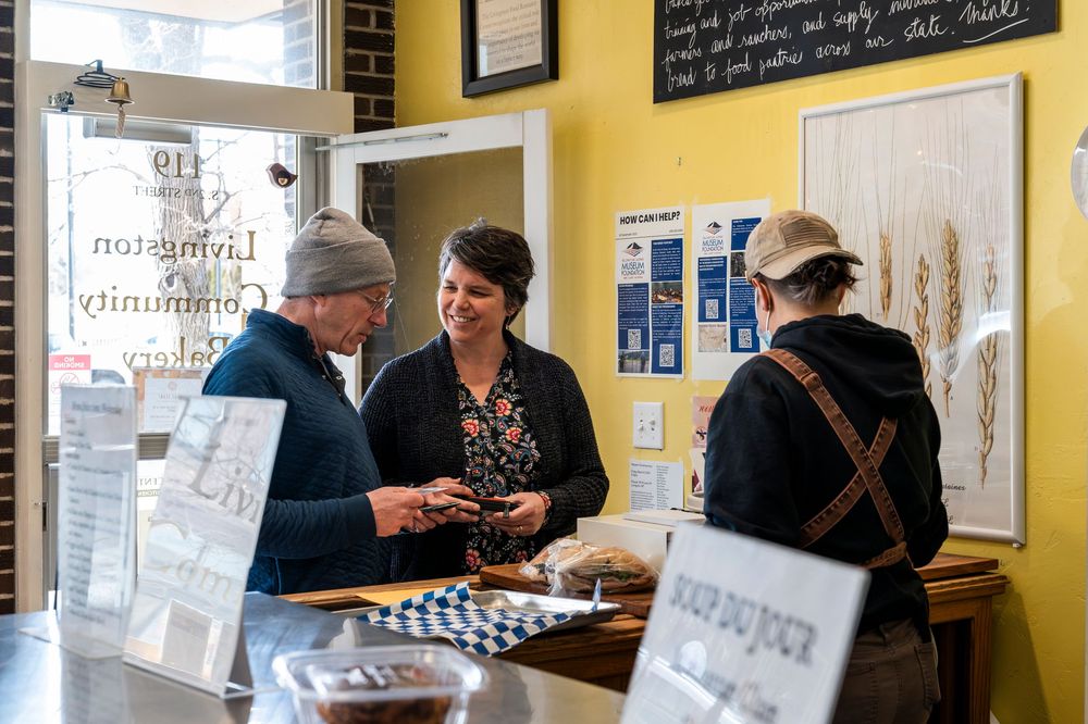 Customers browsing baked goods at a rustic bakery counter with yellow walls.