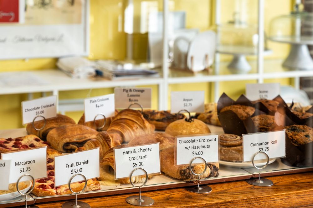 Row of artisanal breads and pastries with descriptive labels in a bakery display case.