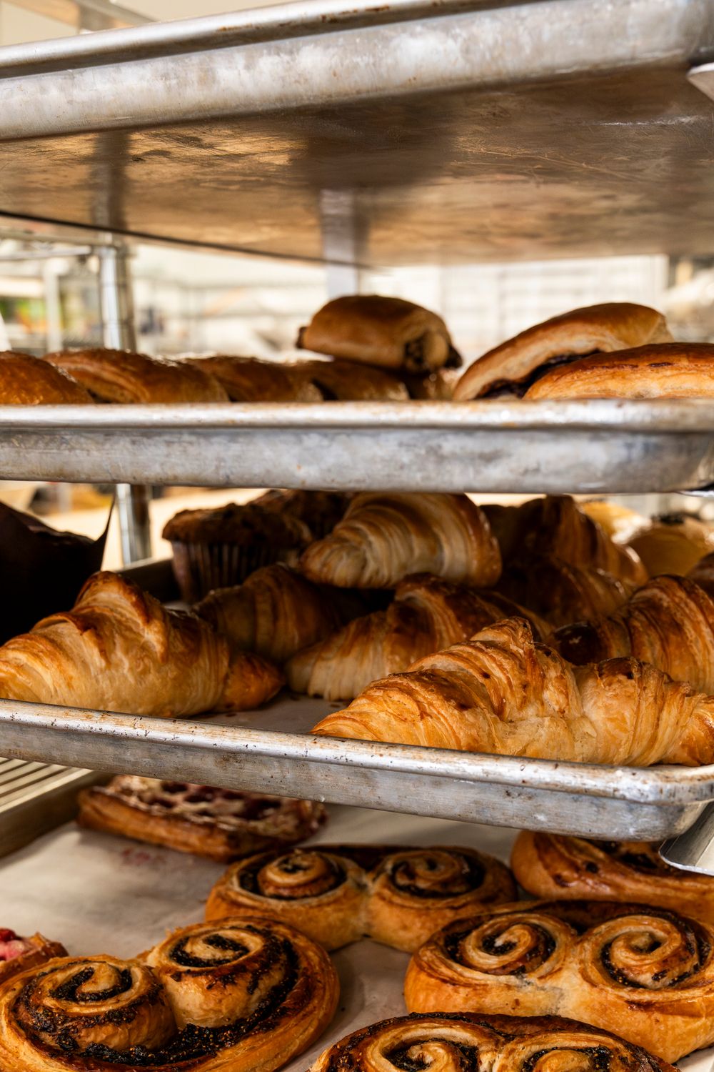 Freshly baked croissants and cinnamon rolls arranged on metal bakery shelves.