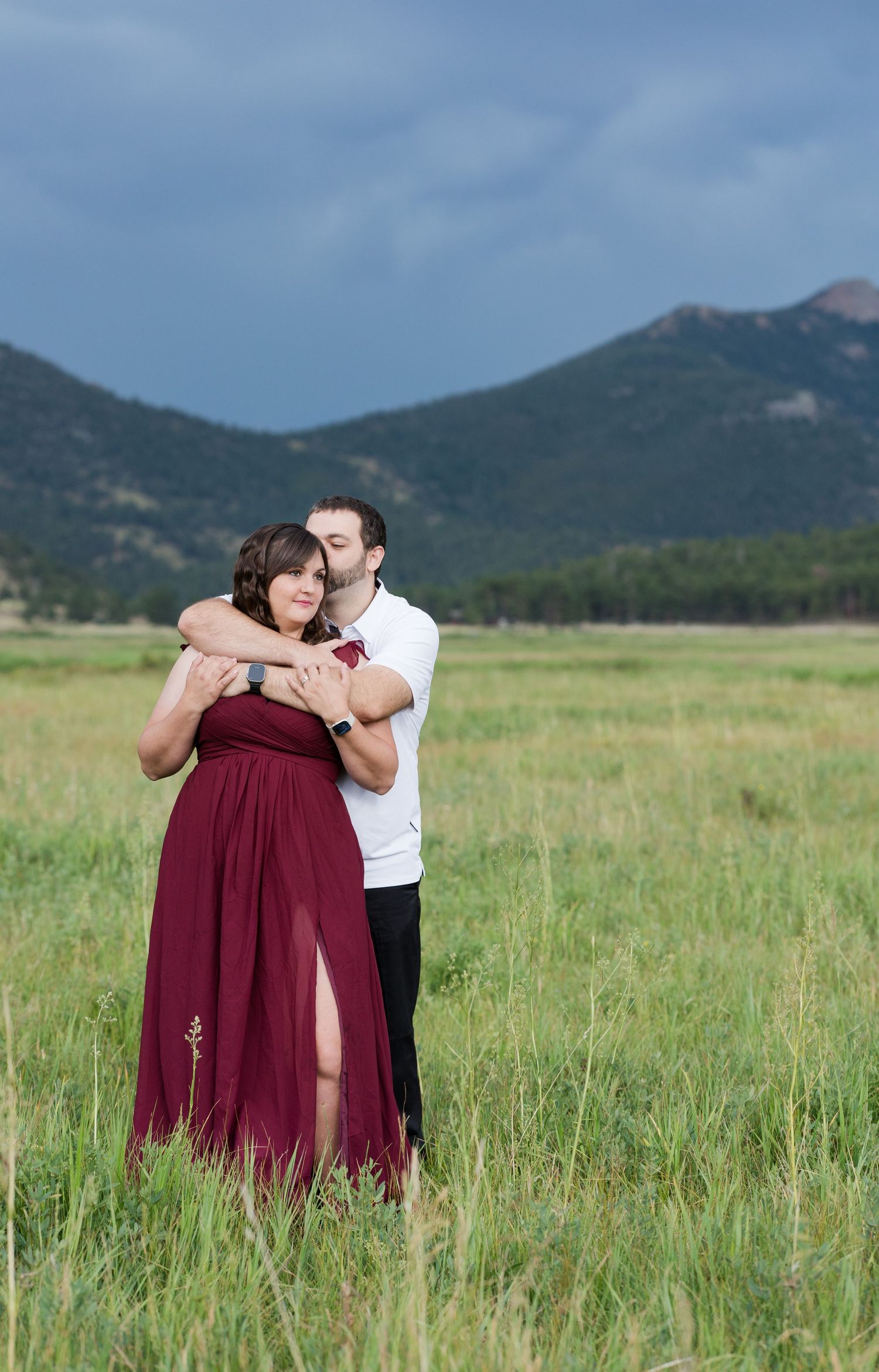 A couple holds hands in a grassy meadow with mountains in the background near Estes Park, Colorado.