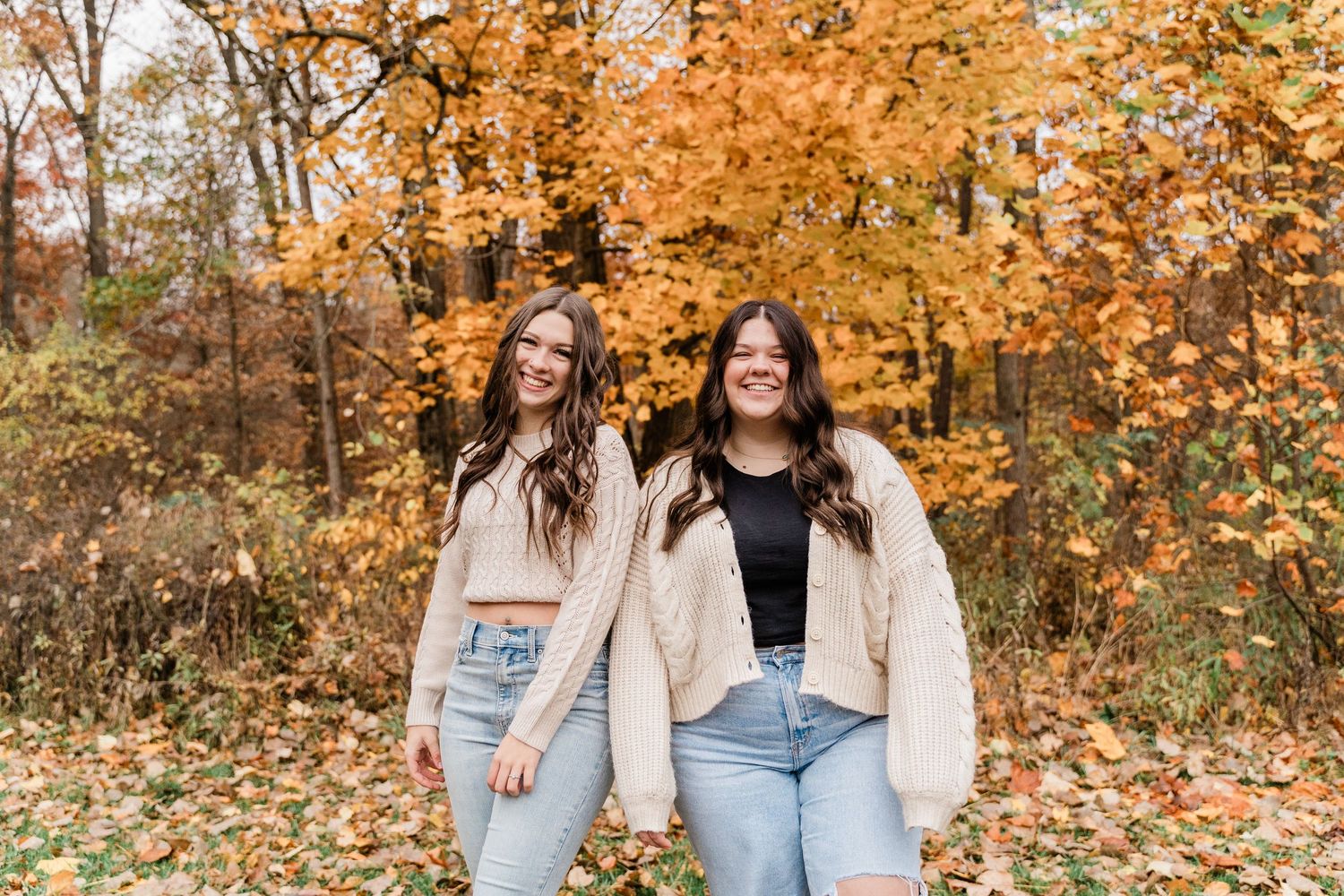 Lake High School seniors in casual fall attire walk together and laugh surrounded by vibrant orange autumn foliage in a forest setting.