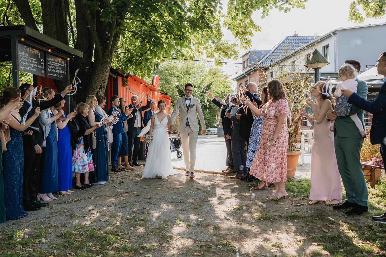 Wedding guests gathered outdoors under trees for a celebration.