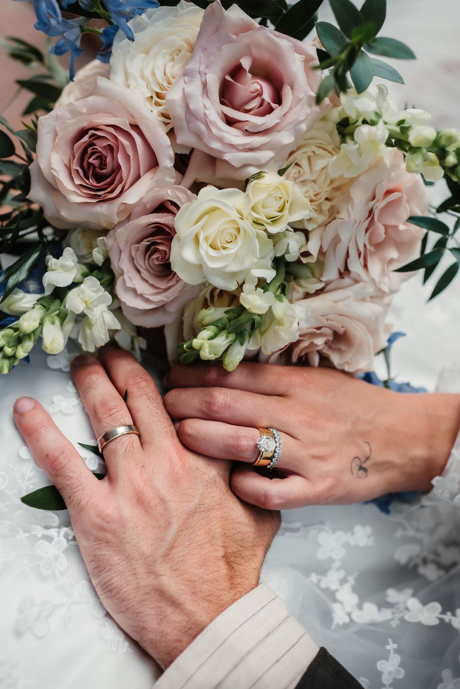 Close-up of hands with wedding rings holding pink and white floral bouquet.