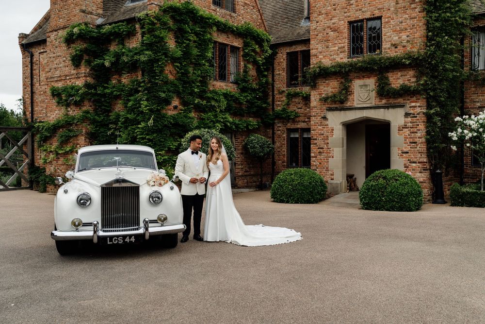 A classic white vintage car parked in front of a rustic brick building during a wedding celebration at The Old Hall Ely.