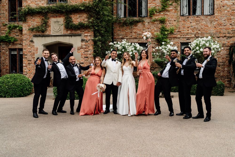 Stylish wedding party poses outside historic brick building in black, white and coral attire.