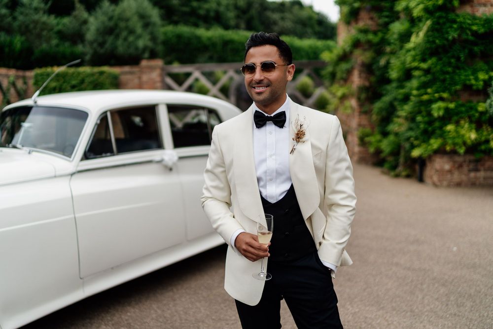 A classic white vintage wedding limousine parked on a gravel driveway during an elegant outdoor celebration.