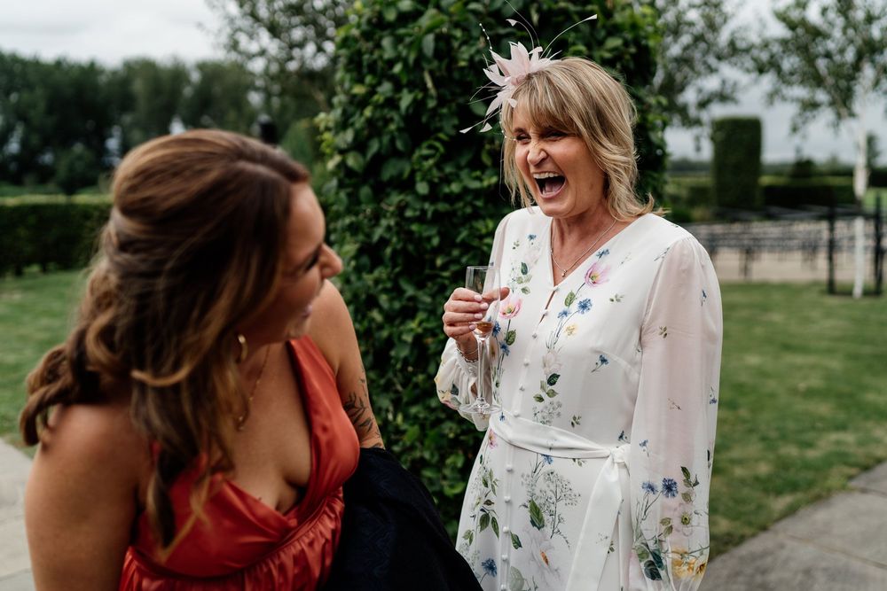 Two women sharing a candid laughing moment together in a garden setting, wearing red and floral summer outfits.