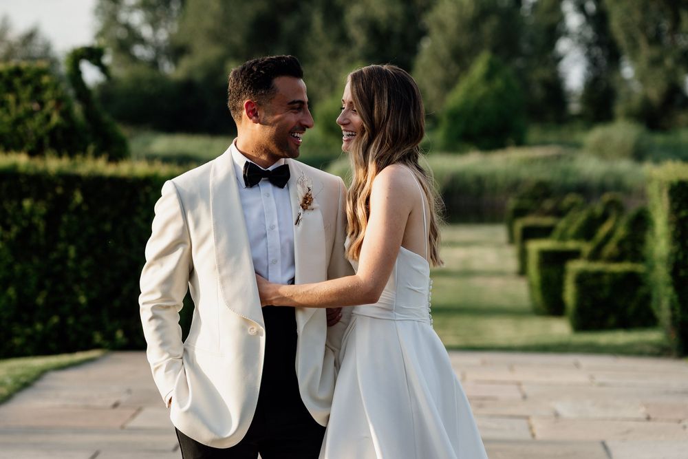 A romantic couple in wedding attire share tender moments while walking through a beautiful outdoor garden setting.