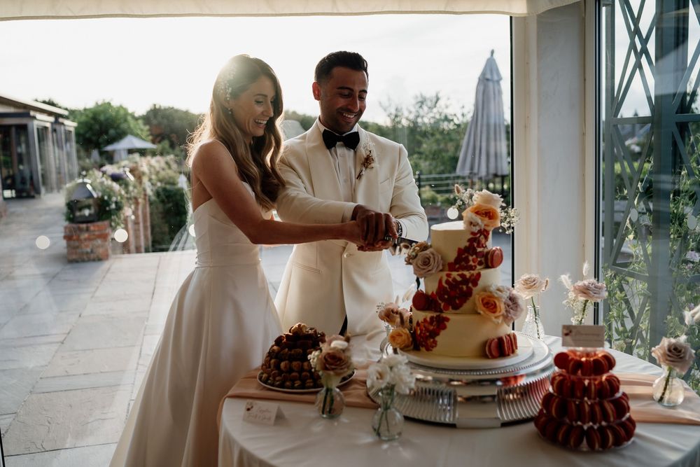A couple in formal wedding attire cutting their three-tiered cake together at The Old Hall Ely.