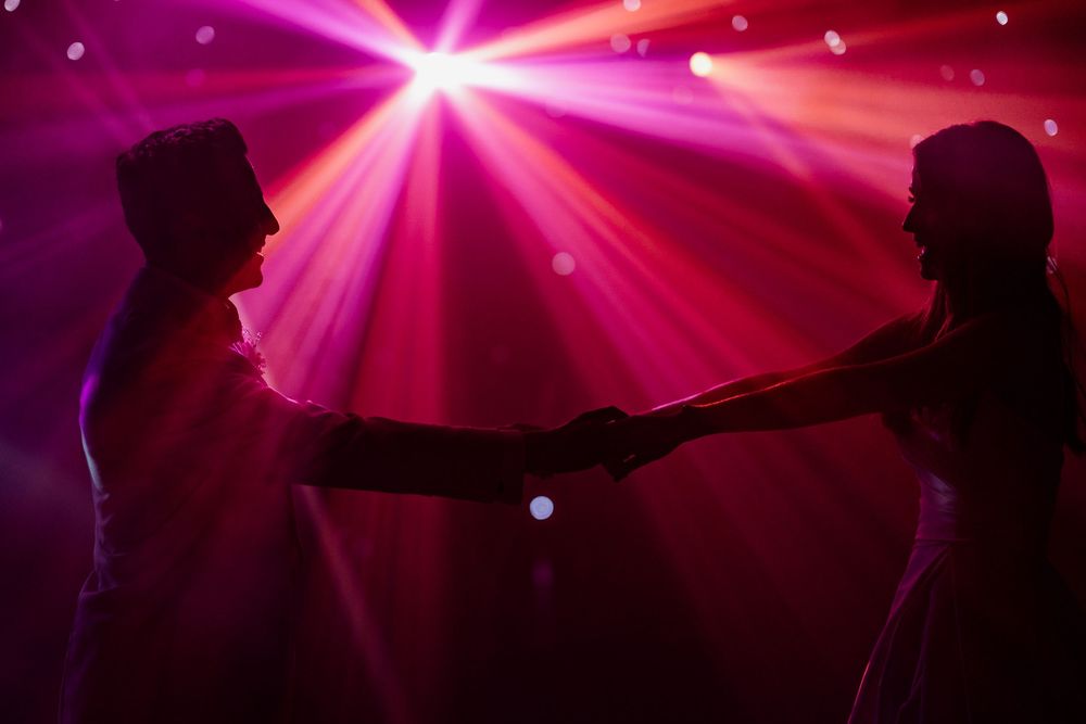 Two silhouetted figures reaching toward each other under bright pink nightclub lights and starburst effects.
