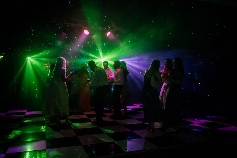 Silhouettes of dancers on a checkered floor under vibrant green laser lights and purple spotlights in The Old Hall, Ely