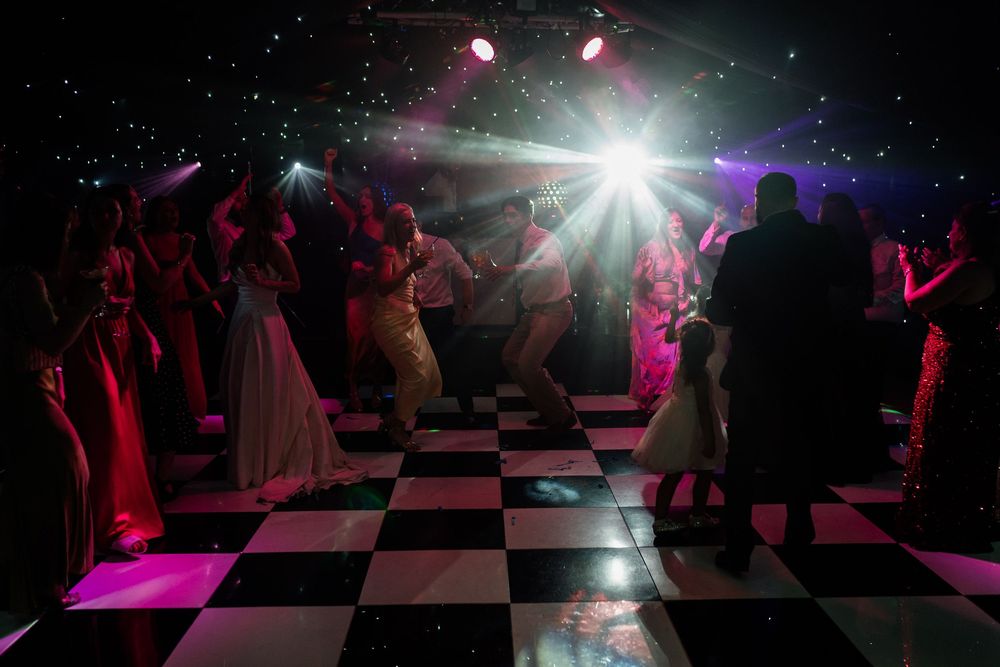Dark dance floor with checkered tiles illuminated by pink and purple lights as people dance at at The Old Hall Ely.
