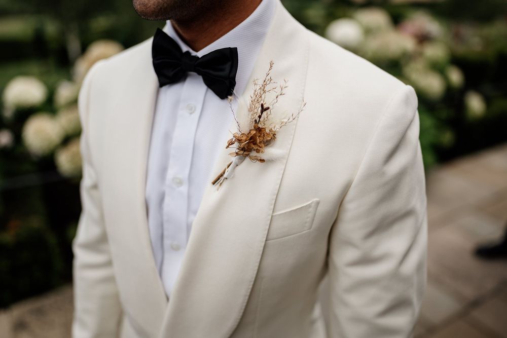 Close up detail of a white tuxedo jacket with black bow tie and dried floral boutonniere.