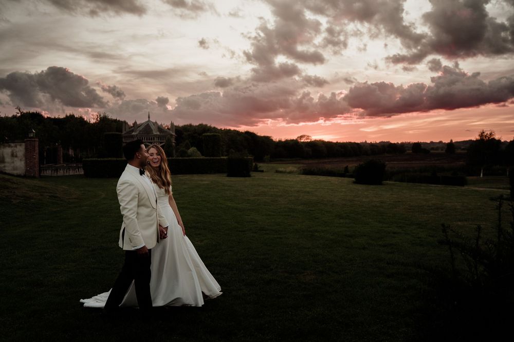 A couple shares a romantic moment at The Old Hall Ely at sunset with dramatic pink and purple clouds in the sky.