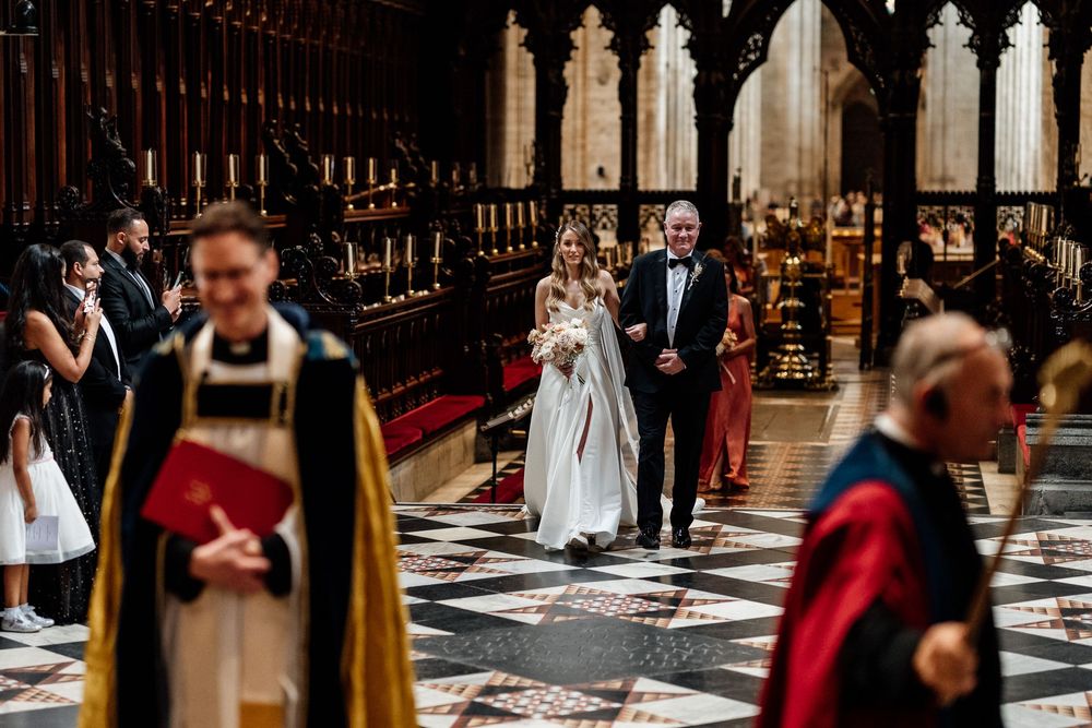 A stunning Gothic Ely cathedral aisle with checkerboard floor and ornate architectural details during a wedding ceremony.