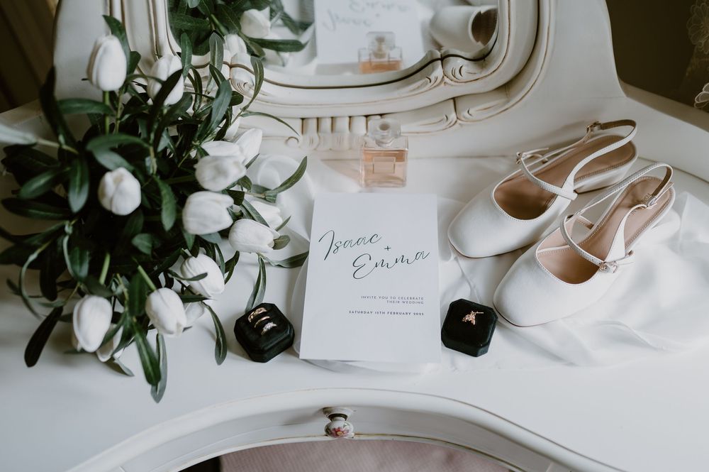 White wedding accessories including stationery, delicate floral arrangements, shoes and decor arranged on a light surface.