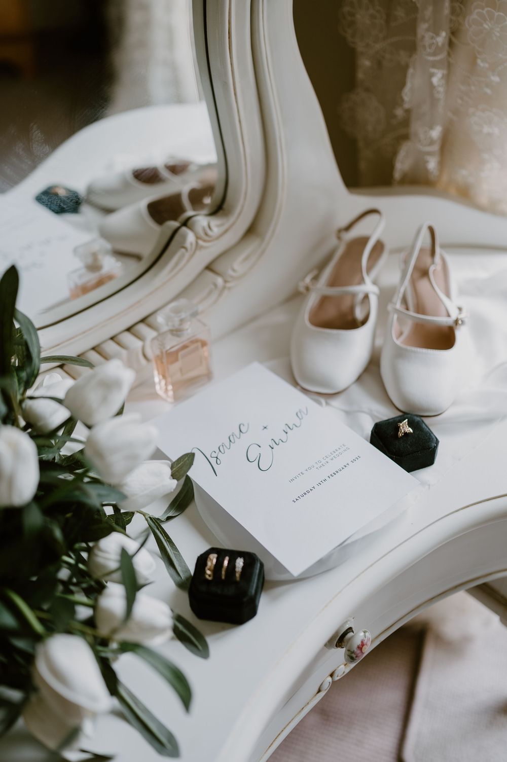 A collection of elegant white wedding shoes arranged with delicate olive branches and handwritten notes on a light surface.