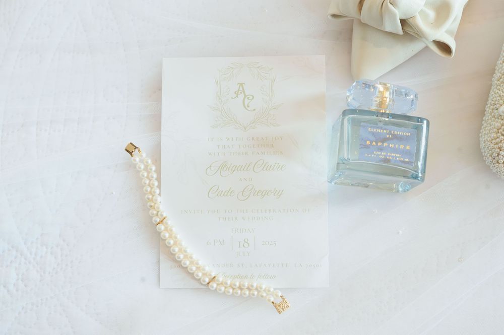 An elegant pearl bracelet and light blue perfume bottle arranged with delicate white fabric and paper on a soft surface.