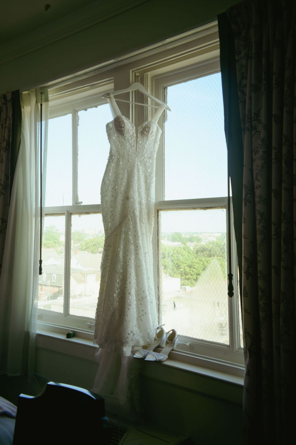 Four window frames displaying a white lace wedding dress hanging gracefully in natural daylight.