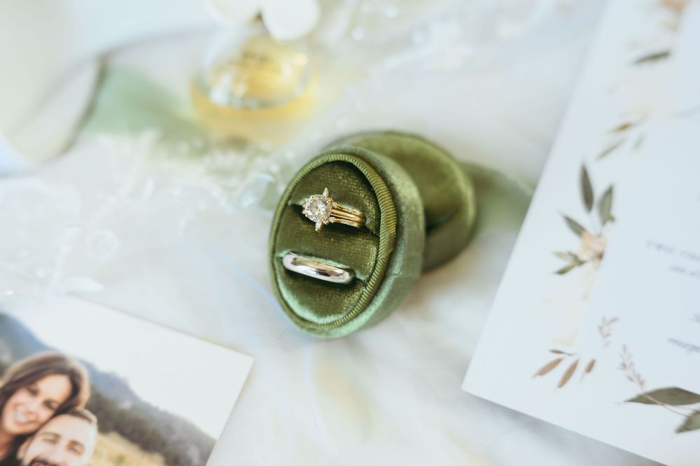 Elegant wedding invitation suite with white envelopes, greenery, and a vintage ring box on a light neutral surface.