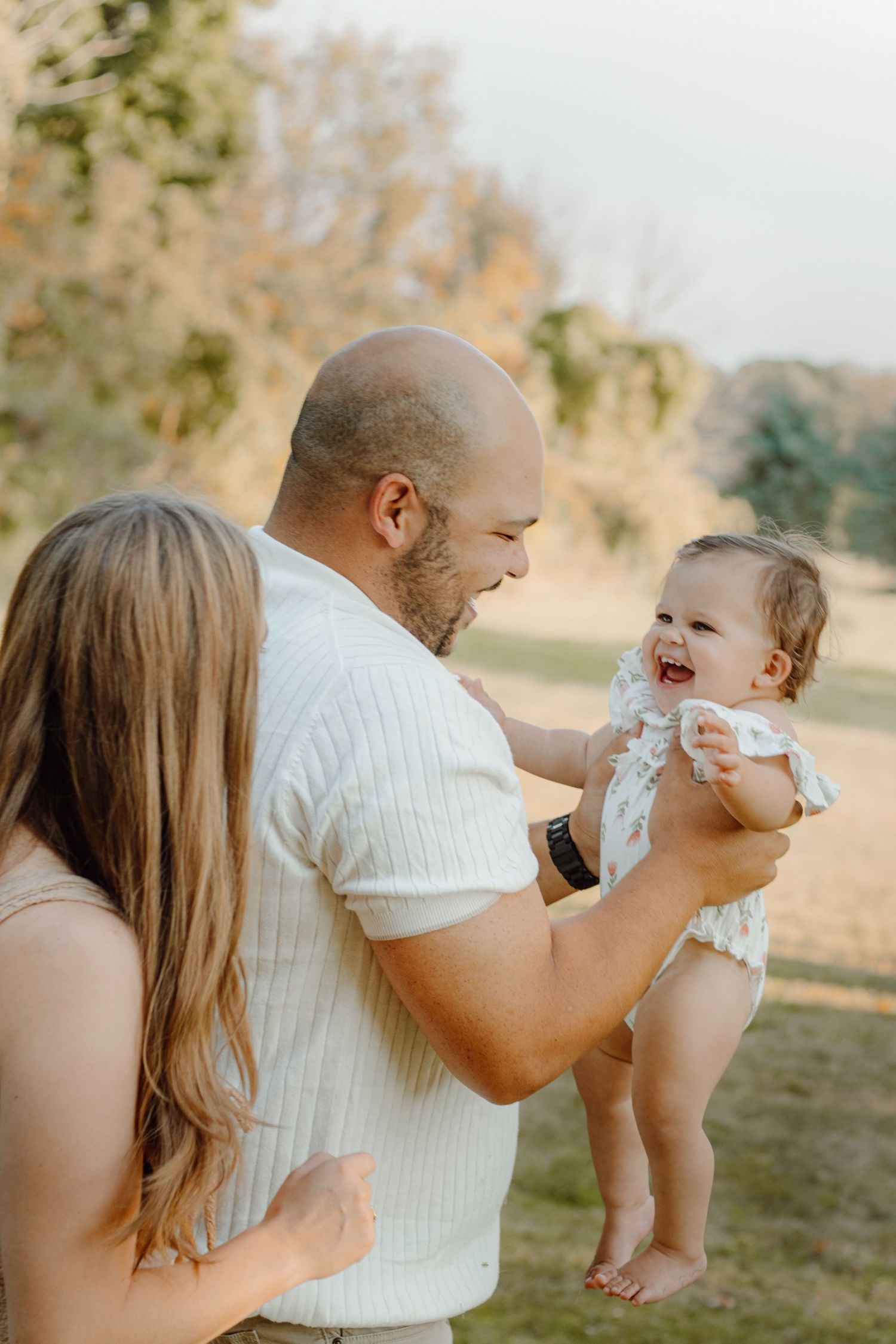 Sweet candid moment of a family laughing together outdoors during golden hour in a natural setting.