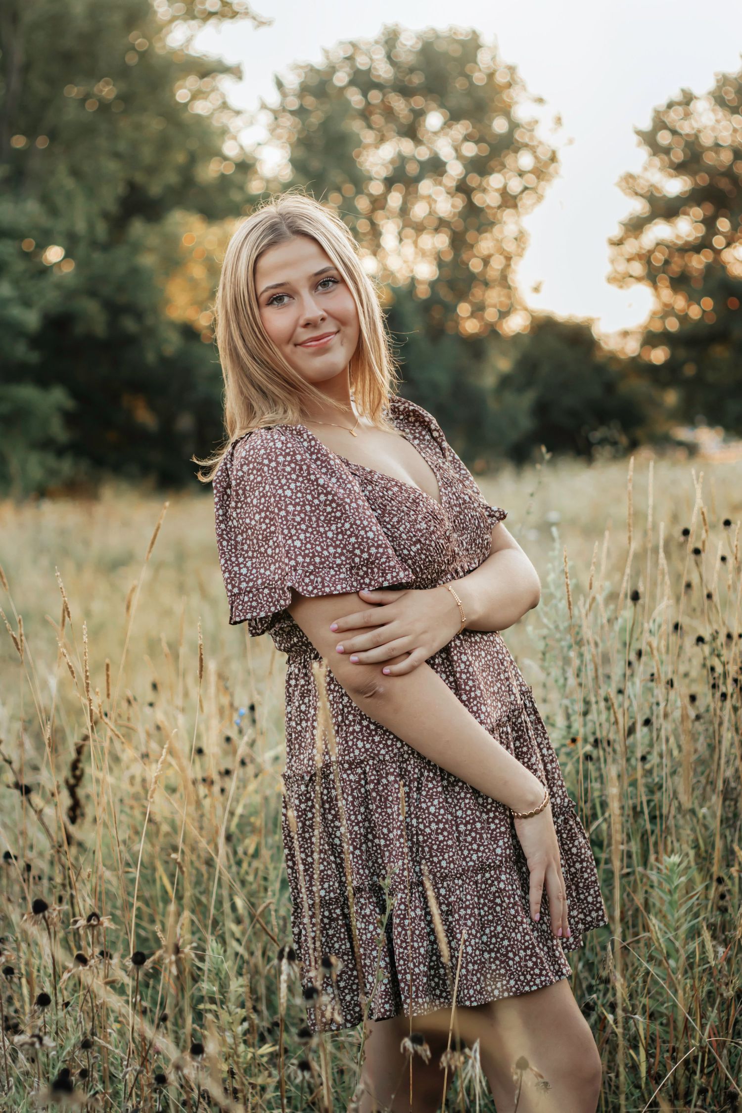 A short-sleeved floral dress catches the warm sunset light in a summer meadow filled with tall dried wildflowers.