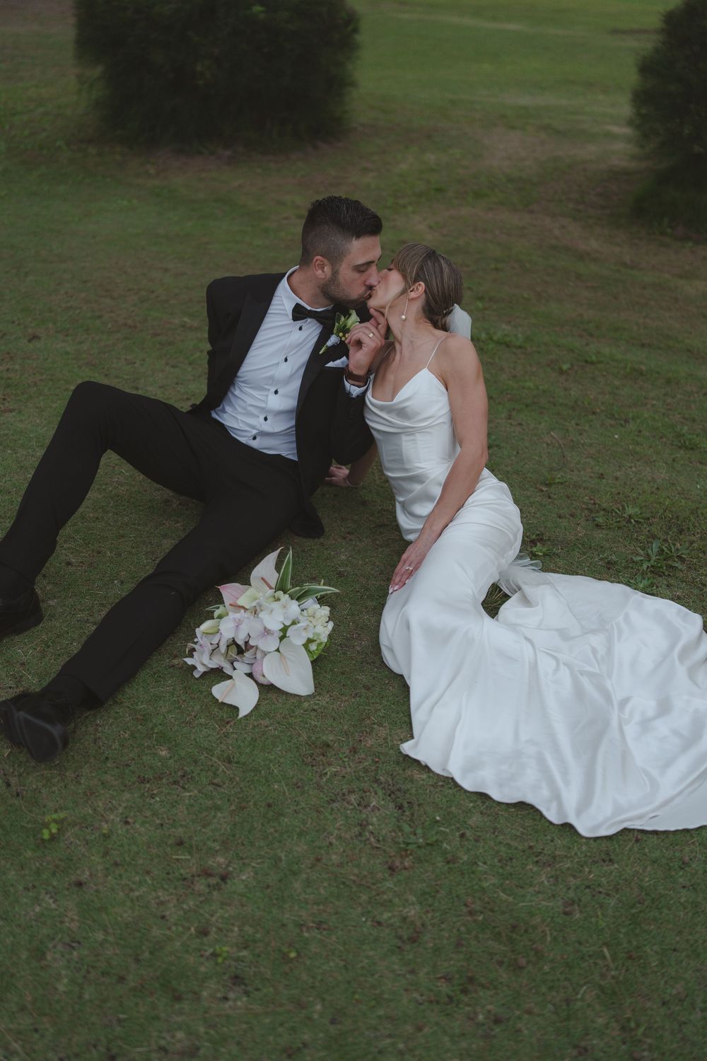 Bride and groom laying in the grass kissing at  Hanalei Bay