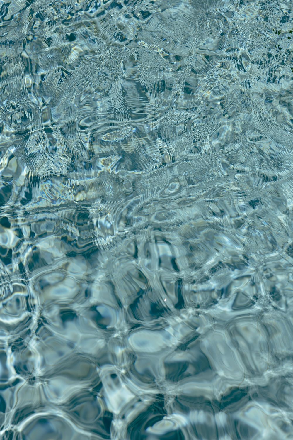 Crystal clear blue pool water with rippling light reflections creating abstract patterns on the surface.