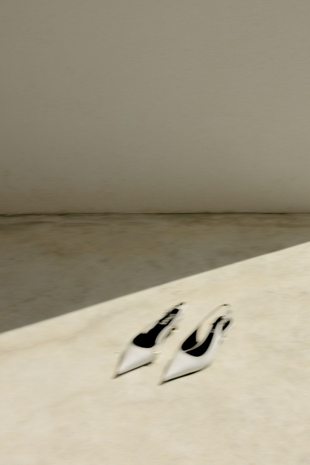 Elegant white pointed-toe slingback heels placed on light stone floor in soft natural light.