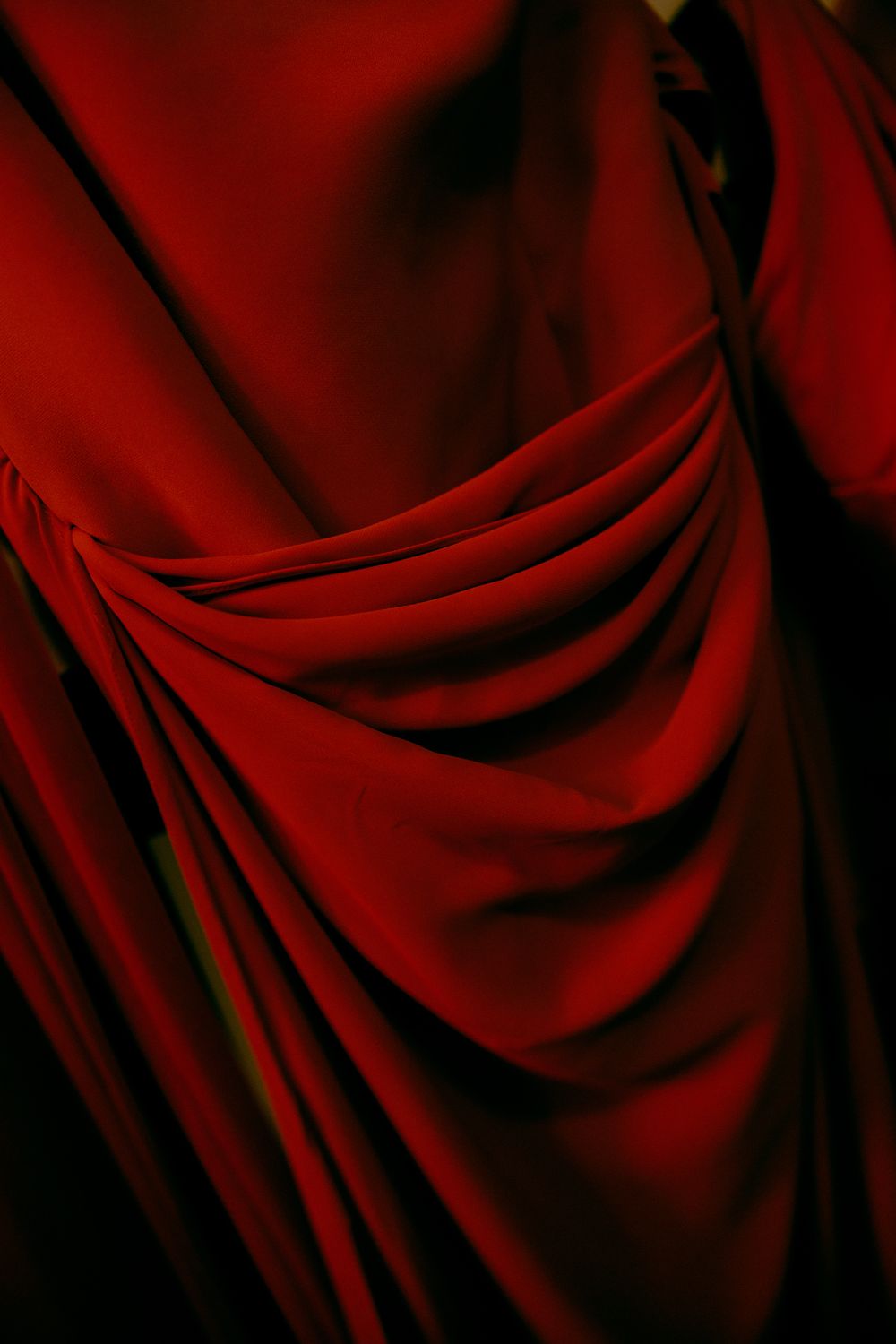 Close-up of rich red draped fabric with deep folds and dramatic shadows.