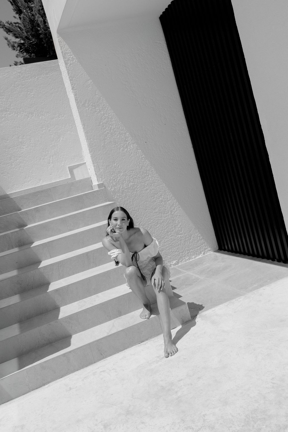 Black and white photo of woman in bikini sitting on white staircase in modern architecture.