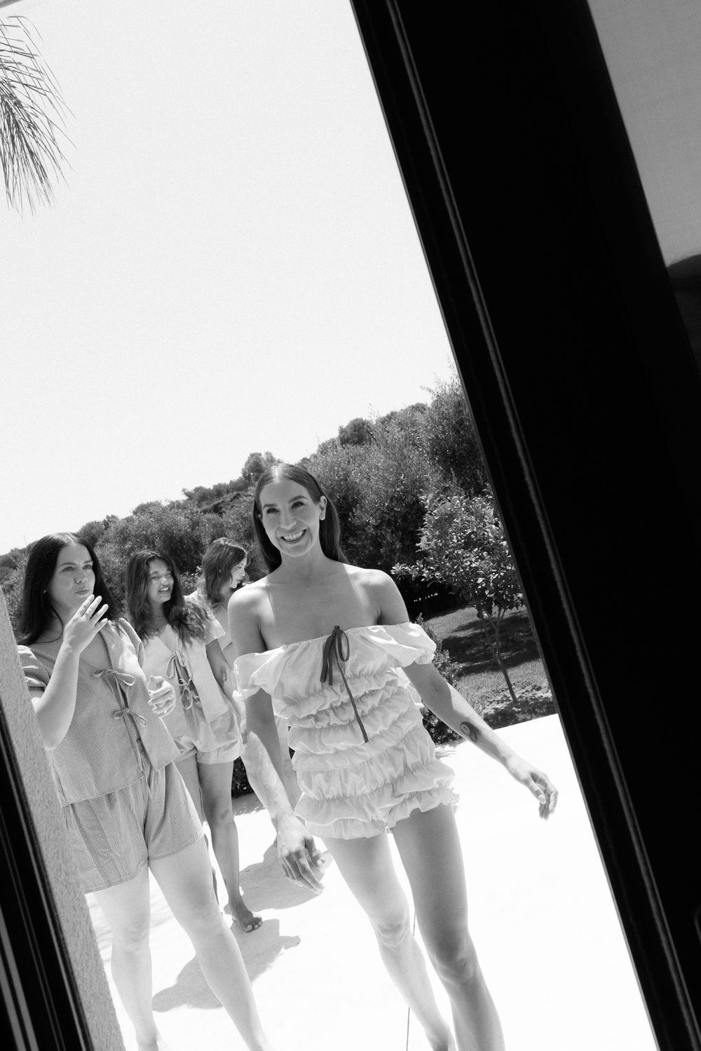 Smiling bride in ruffled mini dress with bridesmaids outdoors.