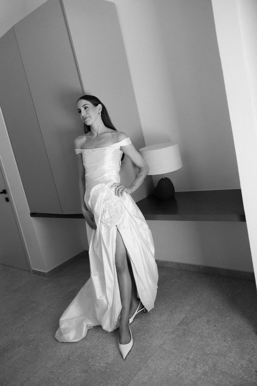 Black and white portrait of a bride in an off-shoulder wedding gown with a thigh-high slit.