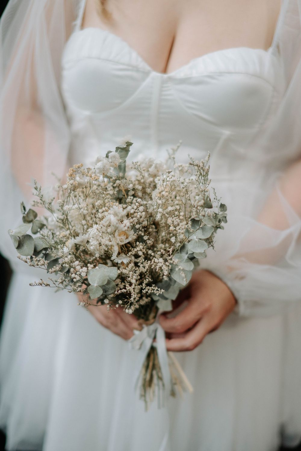 Bride in white sweetheart gown holding elegant dried flower bouquet with eucalyptus and baby's breath.