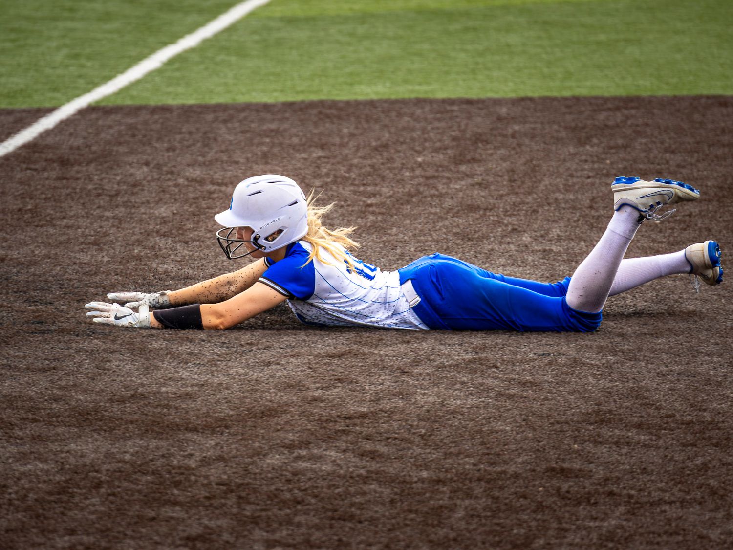 Bryant Hornets softball player in blue uniform sliding headfirst into base on dirt infield during game.