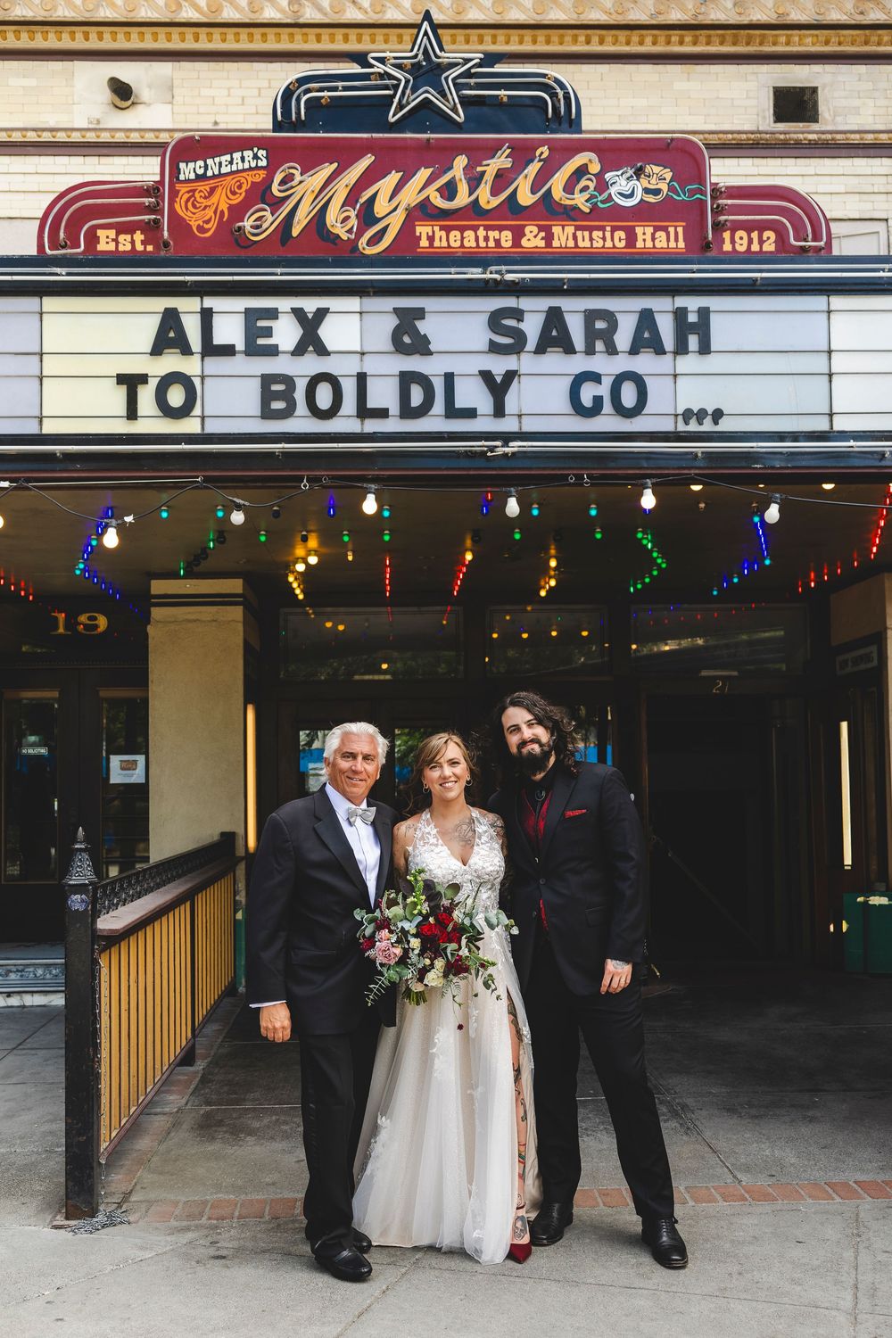 Bride and groom pose with guest outside Mystic Theatre marquee reading Alex & Sarah To Boldly Go.