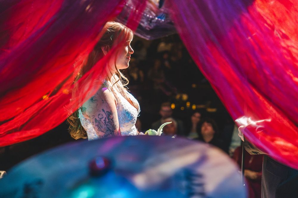 Woman in ornate costume framed by flowing red drapes in a dramatic, colorful event setting.